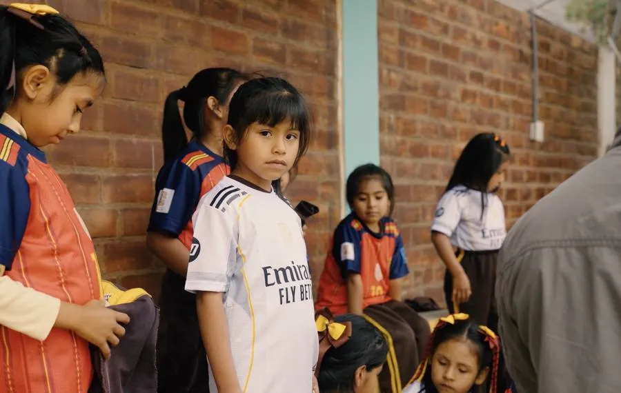 Meisjes in voetbalshirts staan bij de muur van het schoolplein
