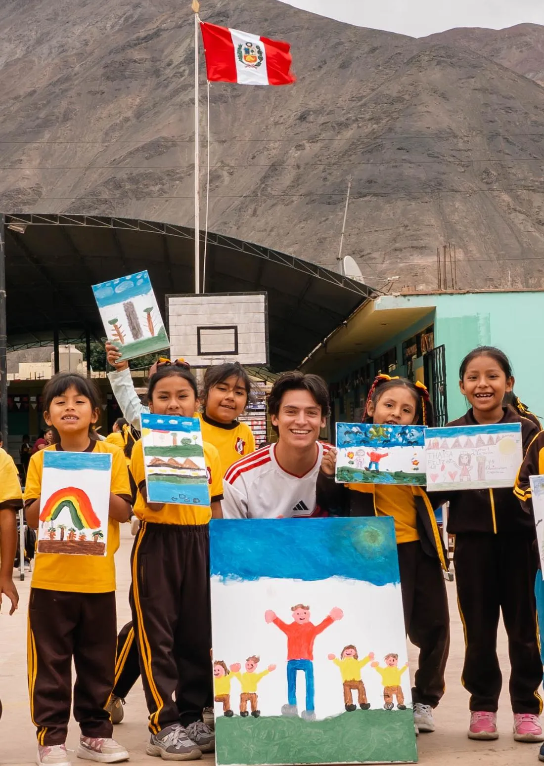 Children proudly show their paintings in the schoolyard, with the Peruvian flag and the mountains behind them